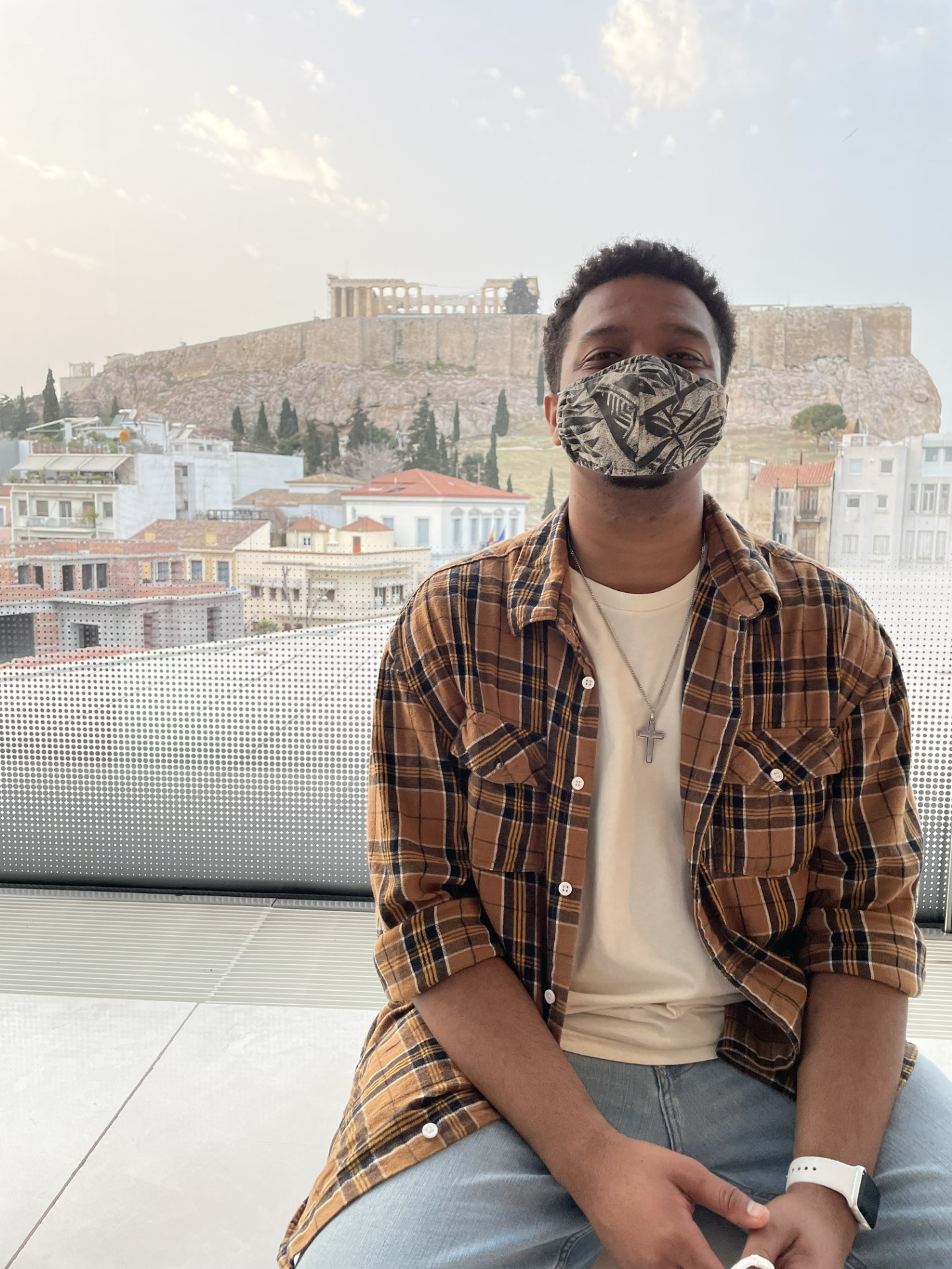 Zion Simpson, wearing a mask, sitting in front of a view in Athens, Greece.